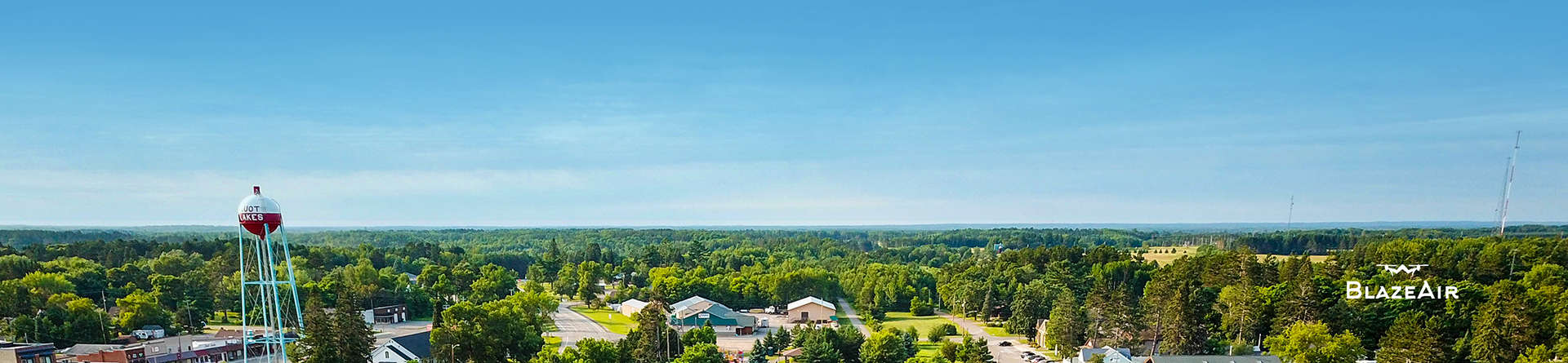 A panoramic photo of the town of Pequot Lakes with bright blue sky and green trees with the bobber tower to the left